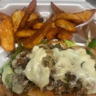Philly cheesesteak with melted cheese and seasoned potato wedges